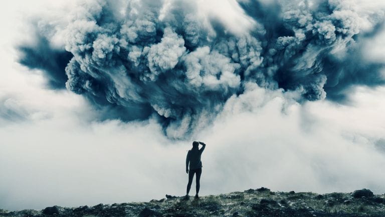 Person watching a vast volcanic ash cloud rise over a volcanic landscape